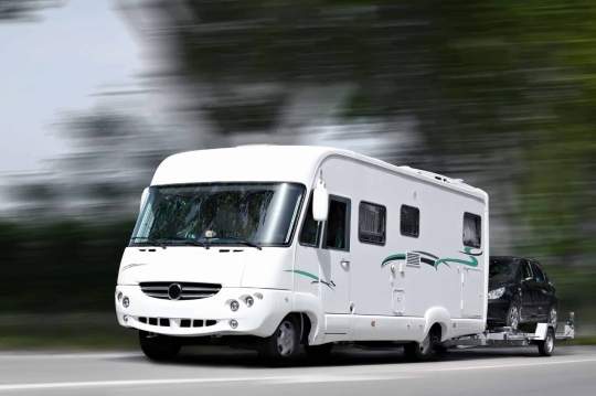 RV traveling down a highway towing an automobile behind