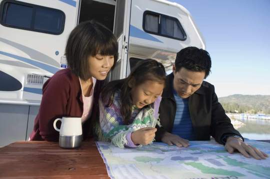 Parents and daughter outside their RV, looking at a map 